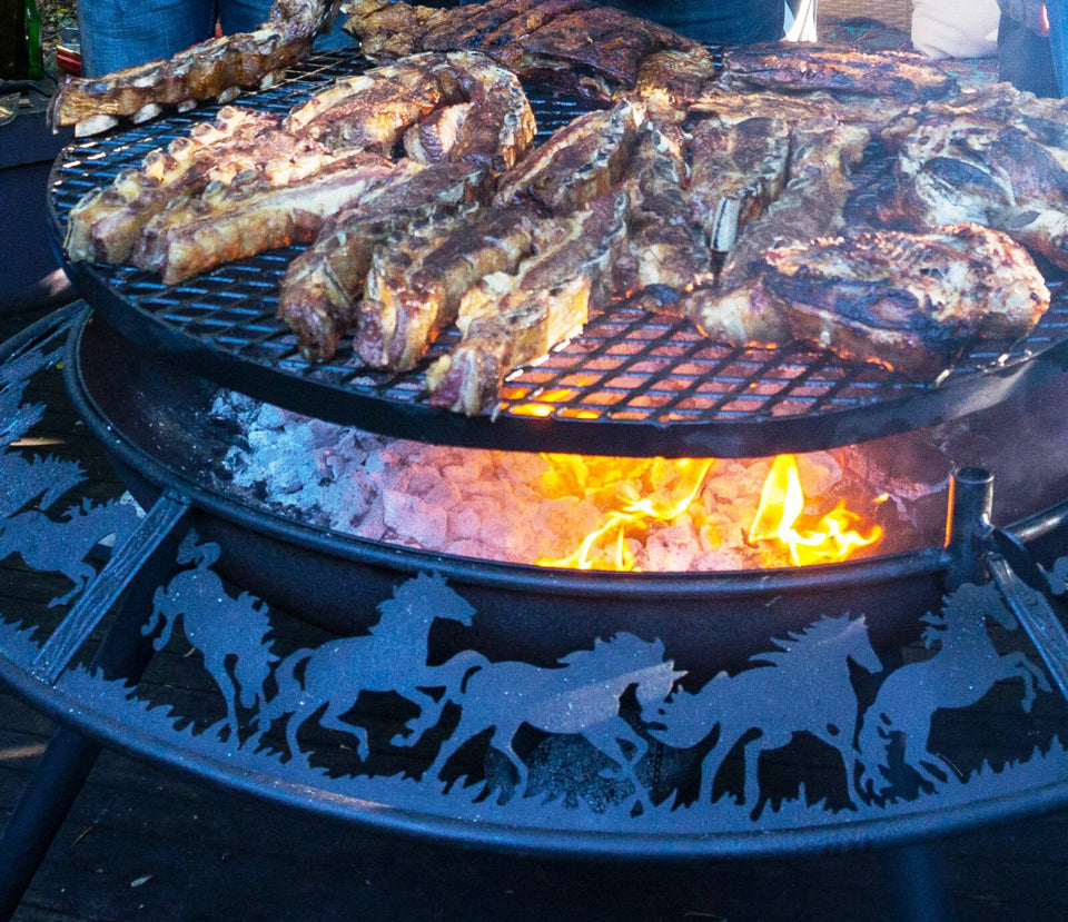 Steaks and ribs cooking on the swinging grill of a BBQ / Fire Pit, coals and flames underneath and galloping horses cut into the rim