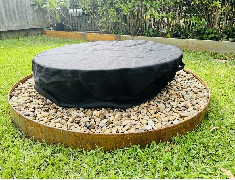 A black vinyl cover pulled over a round fire pit on river stones
